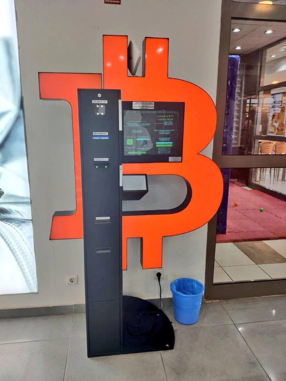 Человек рядом с большим символом биткоина и крипто-терминалом в помещении
